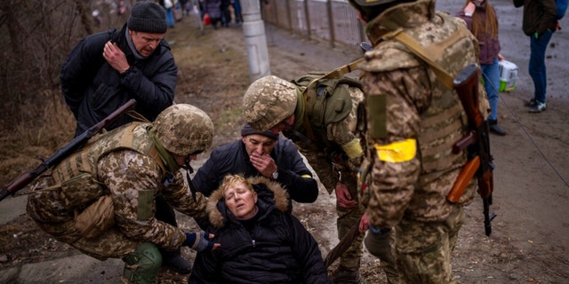 Украинские солдаты ухаживают за женщиной в полубессознательном состоянии после перехода через реку Ирбин во время бегства из города на окраине Киева, Украина, суббота, 5 марта 2022 года. 