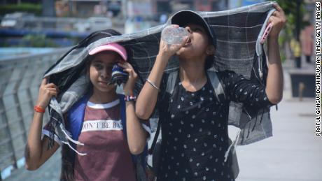 Девушки покрывают головы, когда идут и пьют воду в палящем полуденном зное Мумбаи.