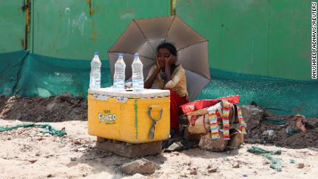 Девушка, продающая воду, использует зонтик, чтобы защитить себя от солнечных лучей в Нью-Дели.