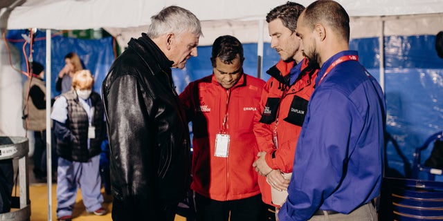 Преподобный Франклин Грэм (слева) молится с группой добровольцев на Украине, помогая людям, чья жизнь была разрушена войной.  На этой неделе Грэм разговаривал с Fox News Digital по телефону.