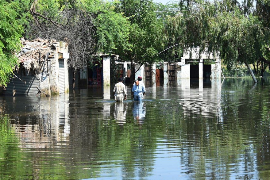 Жители бродят по паводковым водам возле своих домов после проливных муссонных дождей.