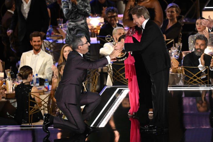 Джон Оливер становится на колени, принимая награду за лучшую серию эстрадных выступлений.