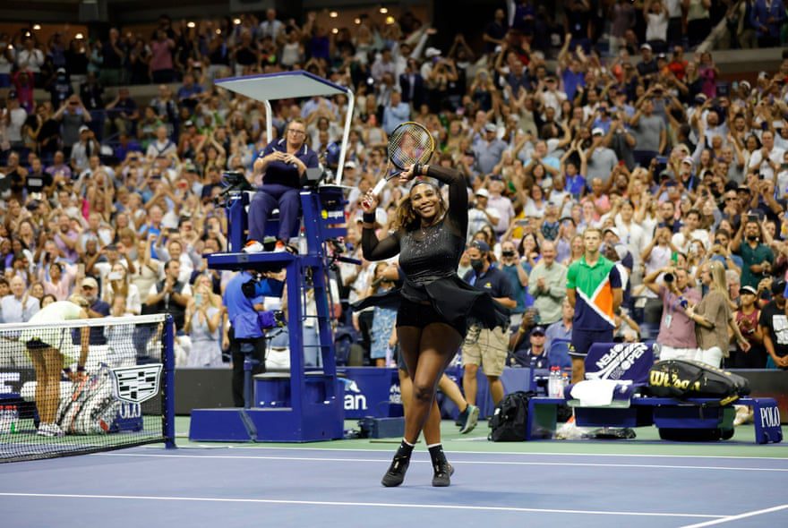 Серена Уильямс поднимает ракетку и руку к толпе, стоя на корте после победы.